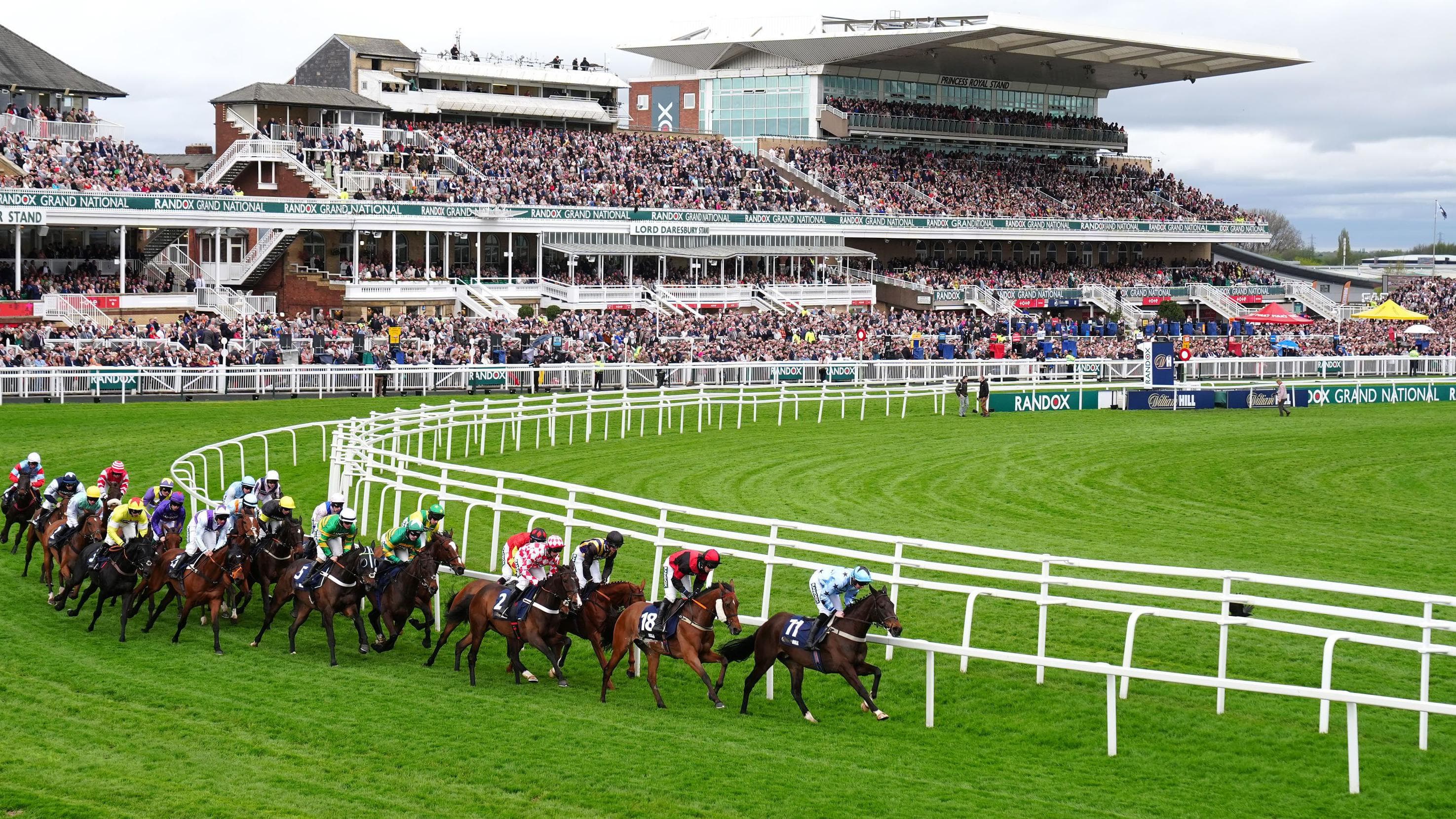 Runners in the Grand National racing in front of the Aintree grandstands.