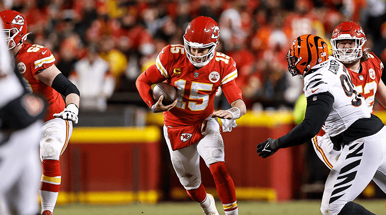 An NFL quarterback scrambling with defenders closing in during a night game.